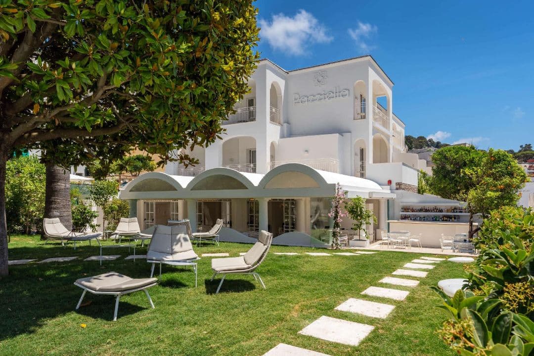 The intimate pool at Pazziella Garden & Suites shaded by a massive ancient magnolia tree with white lounge chairs.