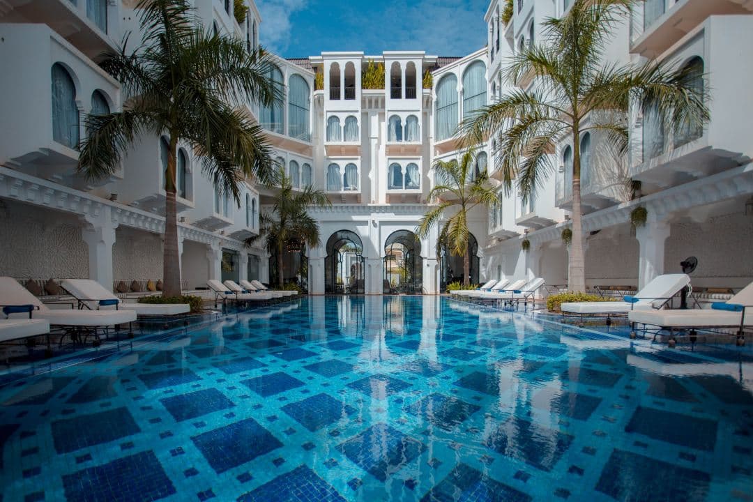 A symmetrical view of the Sarai Resort central pool courtyard framed by white Moroccan arches and hanging lanterns.