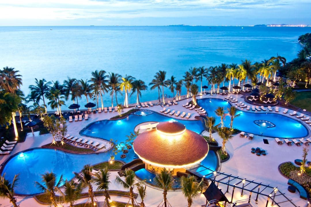 A free-form swimming pool at Royal Wing Suites & Spa with private loungers and ocean views at sunset.