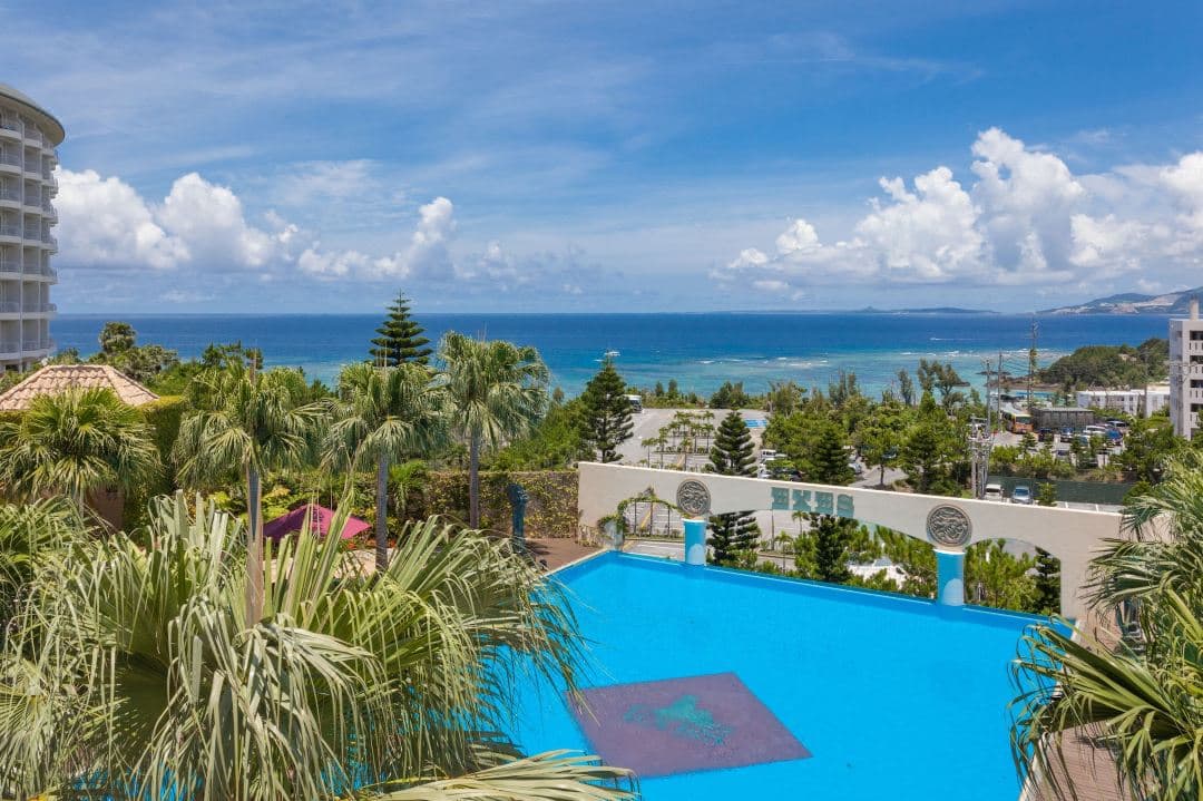 View from a high-floor balcony at Okinawa Kariyushi Resort Exes Onna, showing the curved hotel architecture against a backdrop of the East China Sea at sunset.