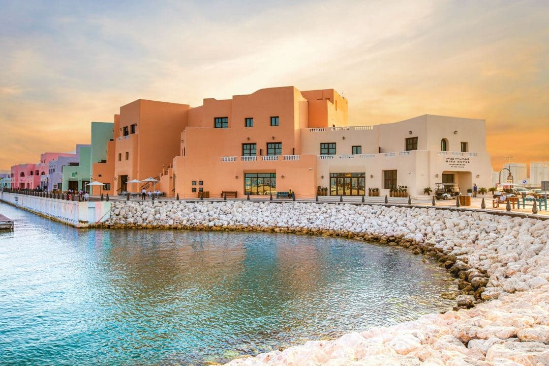 Exterior of Mina Hotel & Residences Doha featuring curved pastel walls and arched windows in the Old Port district.