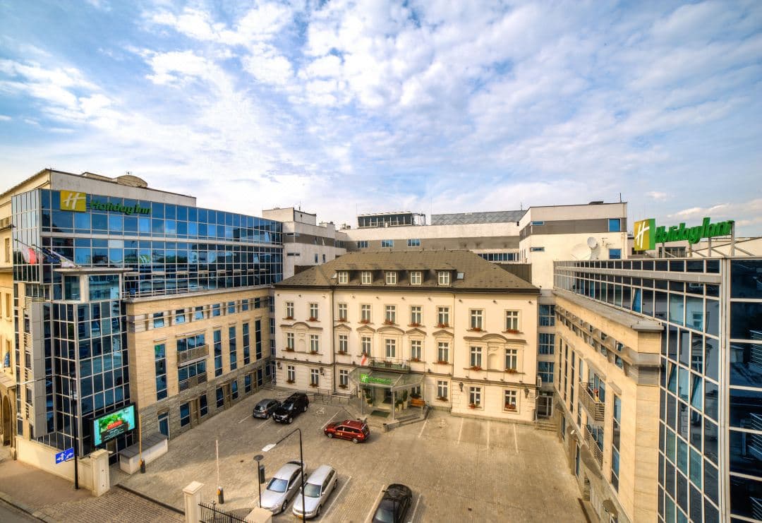 A dramatic glass atrium roof connecting the historic brick walls of the 19th-century Pareński Palace inside the Holiday Inn Krakow.