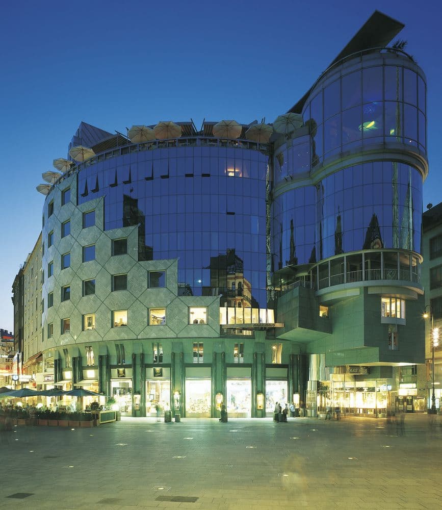 A dramatic view of St. Stephen's Cathedral reflected in the curved glass facade of the DO & CO Hotel Vienna.