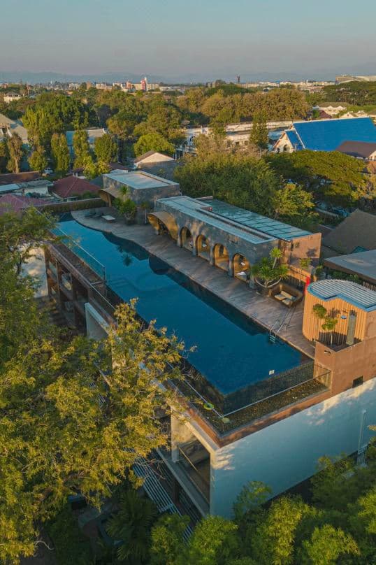 Red brick facade of Cross Chiang Mai Riverside reflecting in the infinity pool at dusk.