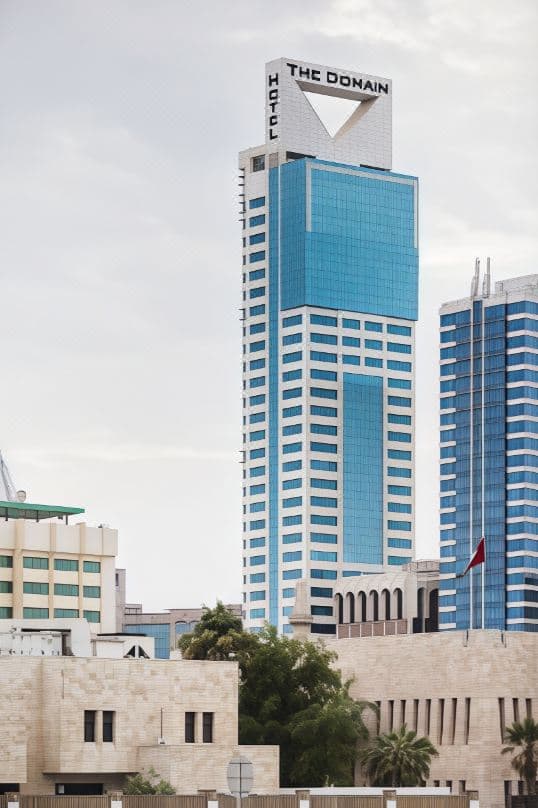A dramatic low-angle shot of The Domain's modern glass facade against a twilight Bahrain sky, emphasizing its height and sleek design.