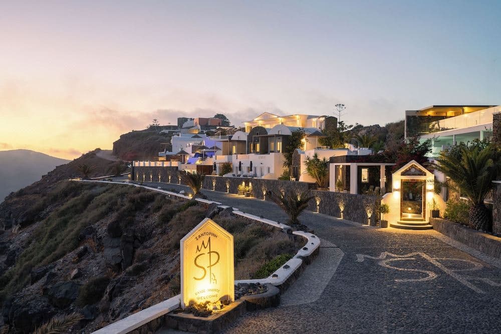 Santorini Princess Spa Hotel infinity pool edge at sunset with Skaros Rock in the background and caldera cliffs.