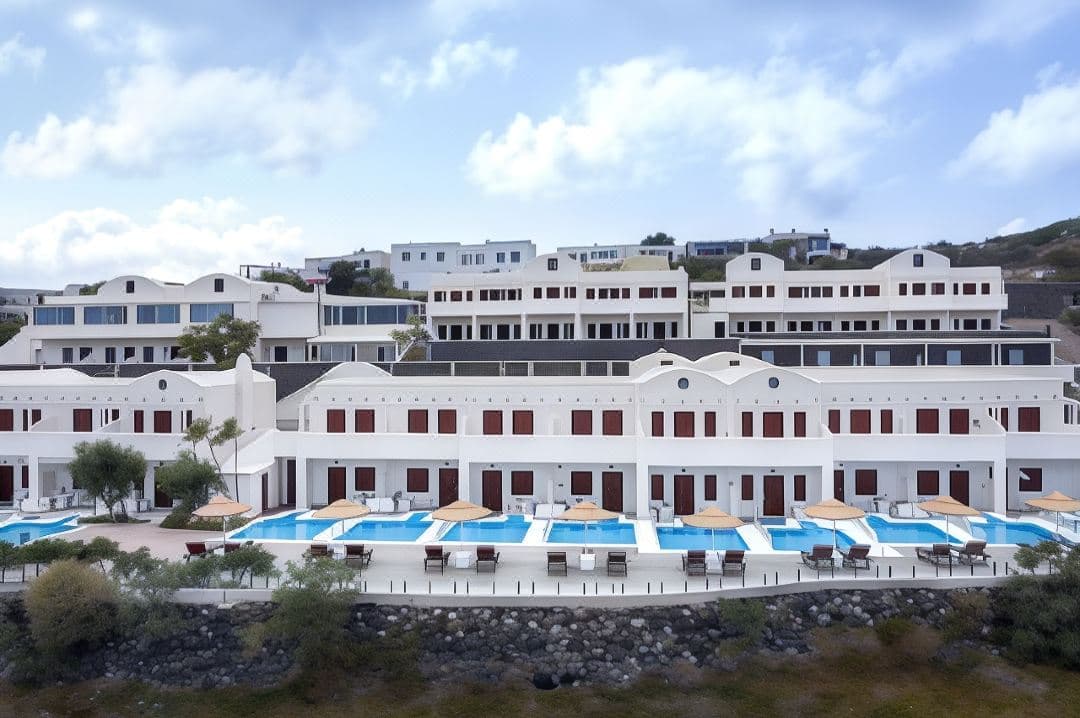Aerial view of Splendour Resort's two-level swimming pool in Firostefani, surrounded by white Cycladic buildings and sun loungers.