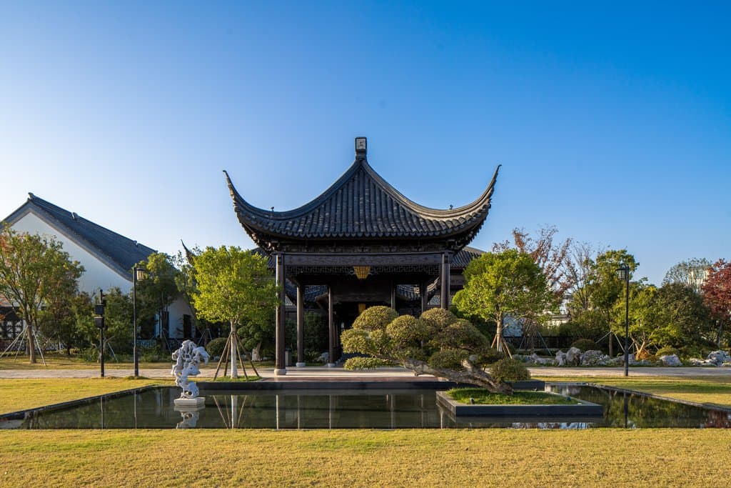 A traditional Song Dynasty style pavilion at The Hanyu Garden Reserve Suzhou reflecting perfectly in a calm central courtyard pond surrounded by manicured pines.