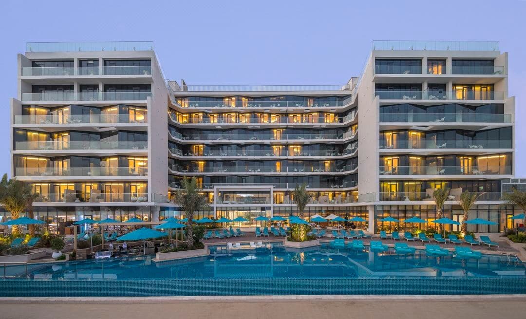A woman relaxing on a sunken lounger in the temperature-controlled infinity pool at The Retreat Palm Dubai, with the Burj Al Arab visible in the distance.