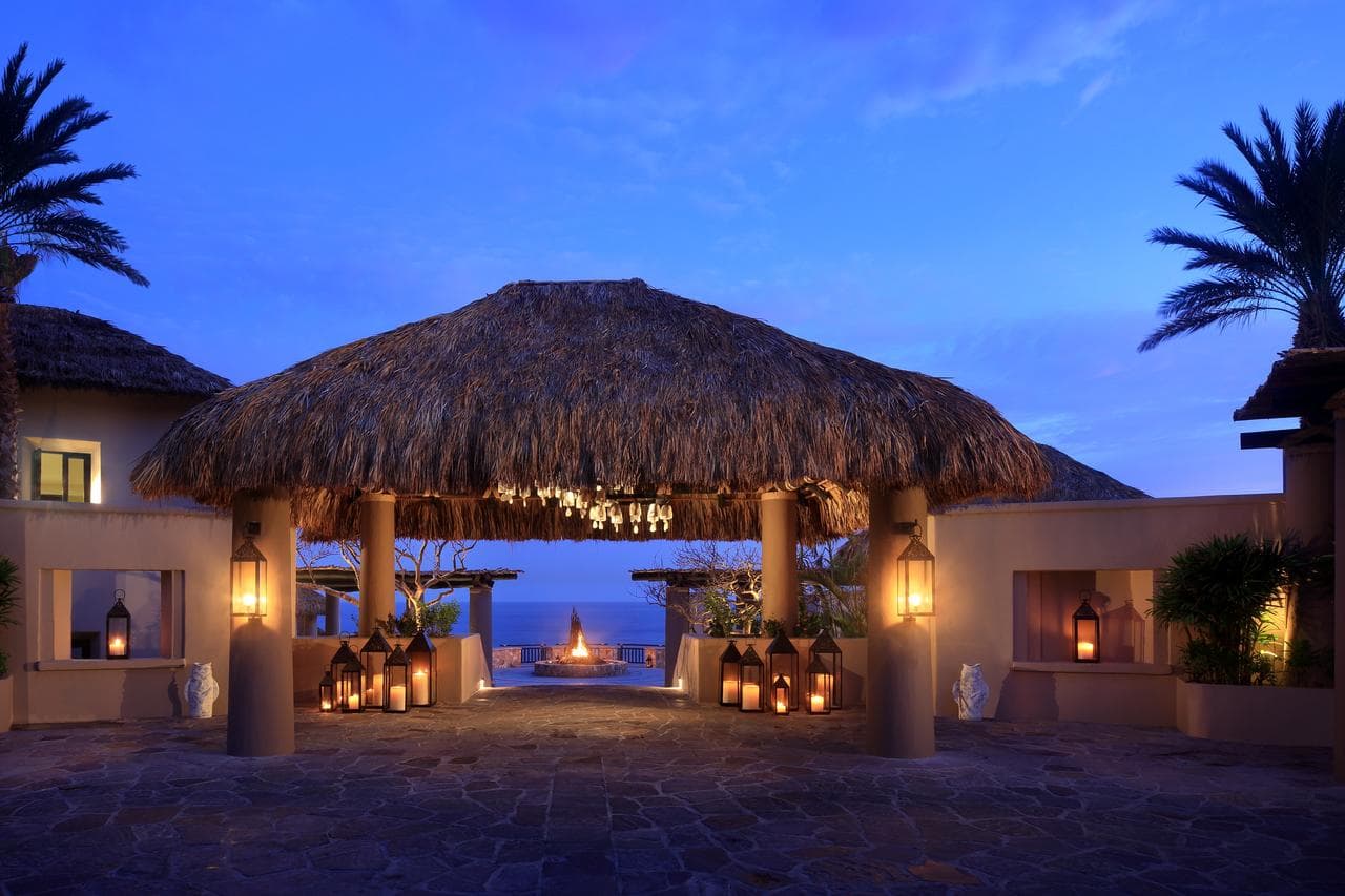 Cocina del Mar restaurant at Esperanza resort at twilight, featuring lantern lighting and tables perched on a rocky cliff over the ocean.