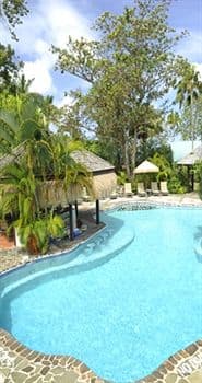 A guest mixing a drink at the self-service swim-up bar in the Bamboo Lounge, surrounded by lush gardens and rattan furniture.