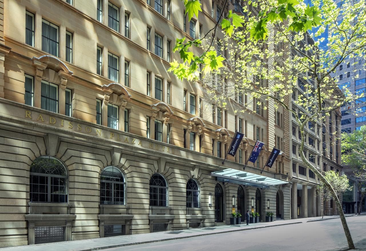 Exterior of Radisson Blu Plaza Sydney featuring heritage sandstone arches and flatiron architecture at street corner.