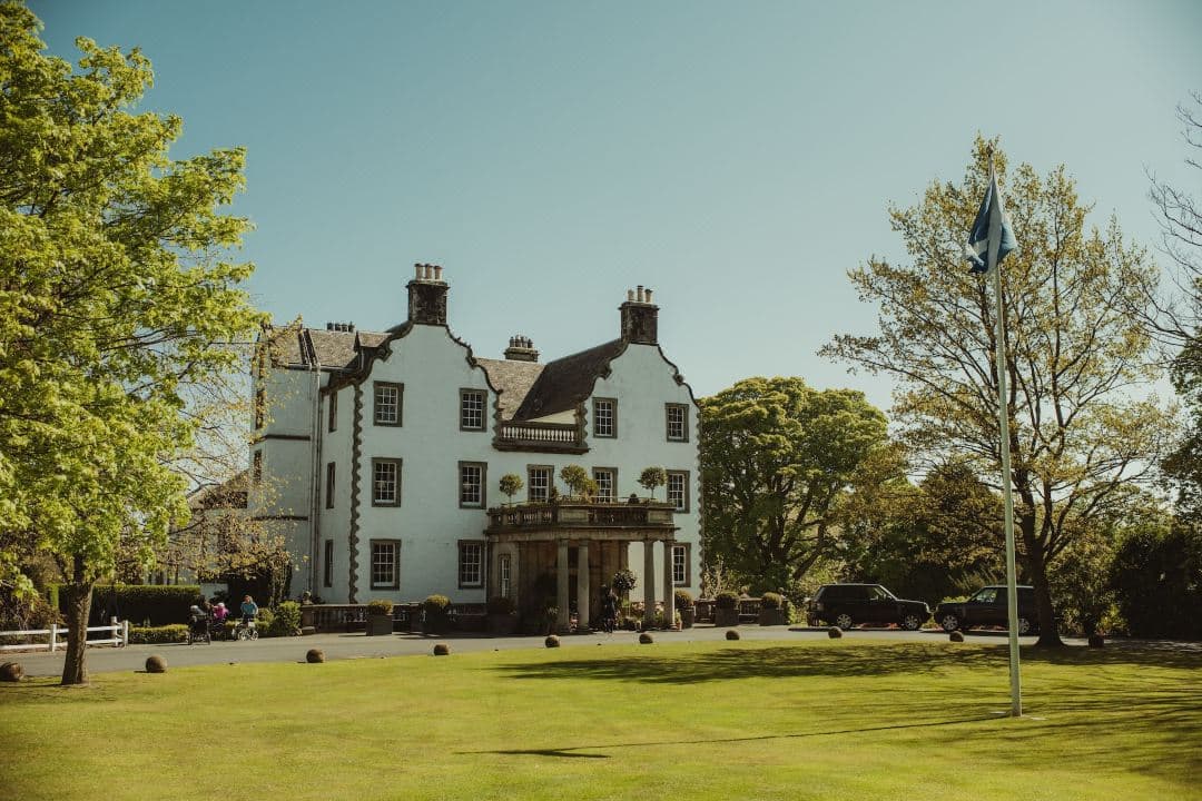 A dramatic baroque hotel room at Prestonfield House featuring dark velvet walls, antique furniture, and a view of Highland cows on the lawn.