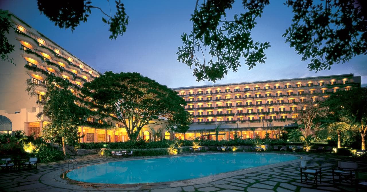 A massive 120-year-old Raintree shading the central courtyard and pool of The Oberoi Bengaluru, surrounded by white balconies.