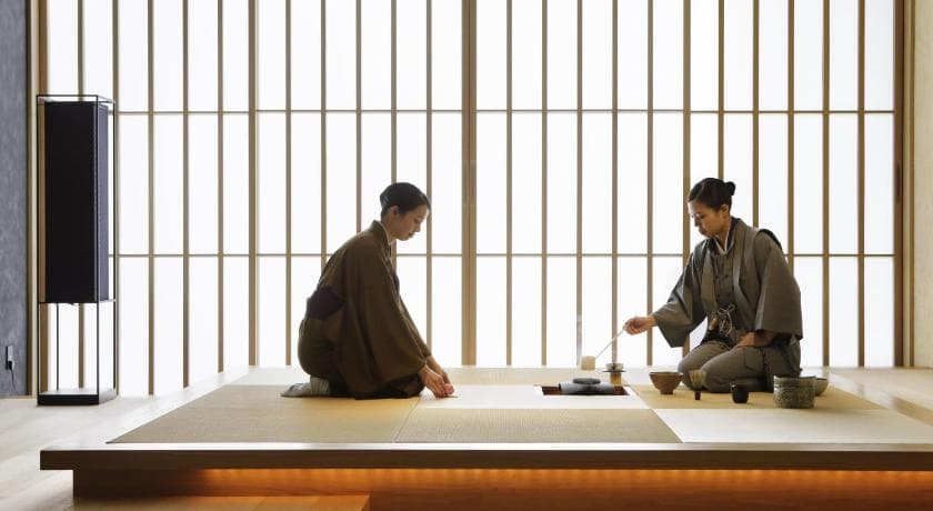 A guest in a kimono walking down a tatami-matted hallway lined with shoji screens at HOSHINOYA Tokyo.