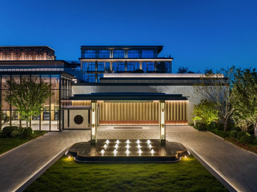 A tranquil twilight view of the Four Seasons Suzhou infinity pool with the illuminated Gate of the Orient skyscraper in the distance.
