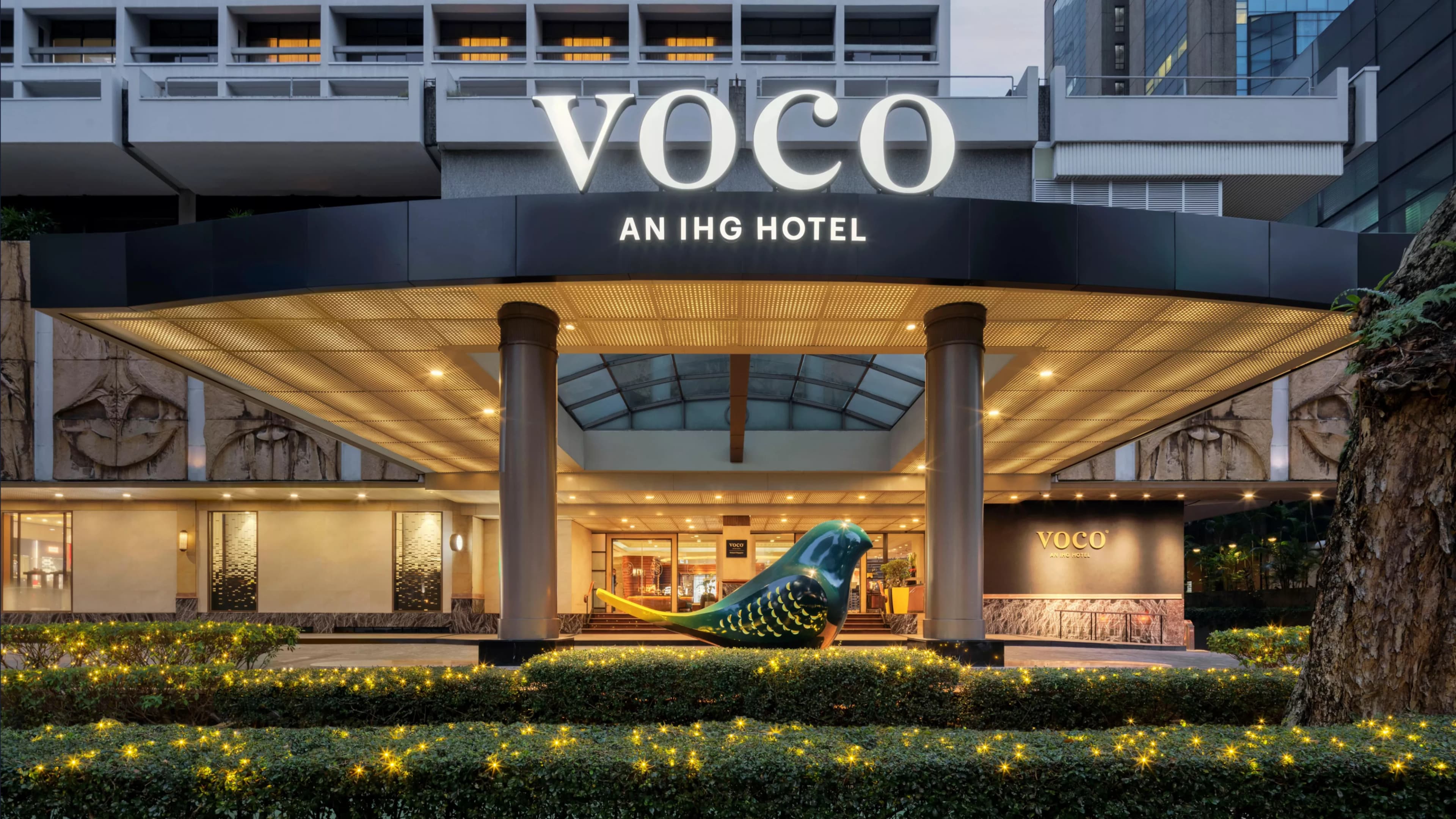 A stylized yellow and teal Finch bird sculpture in the lobby of voco Orchard Singapore, set against modern dark interiors.