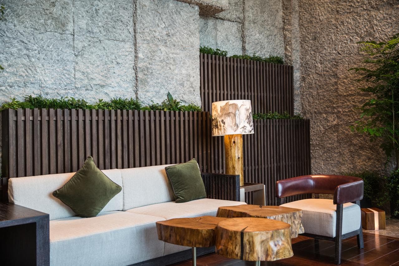 A sleek, minimalist hotel lobby with curved walls, green textured stone, and a serene water feature reflecting soft lighting.