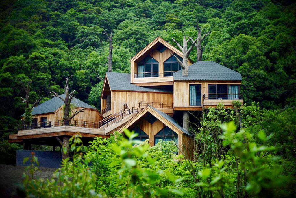 Exterior view of Senbo Resort Hangzhou featuring geometric wooden treehouses stacked on a hillside surrounded by lush green forest.