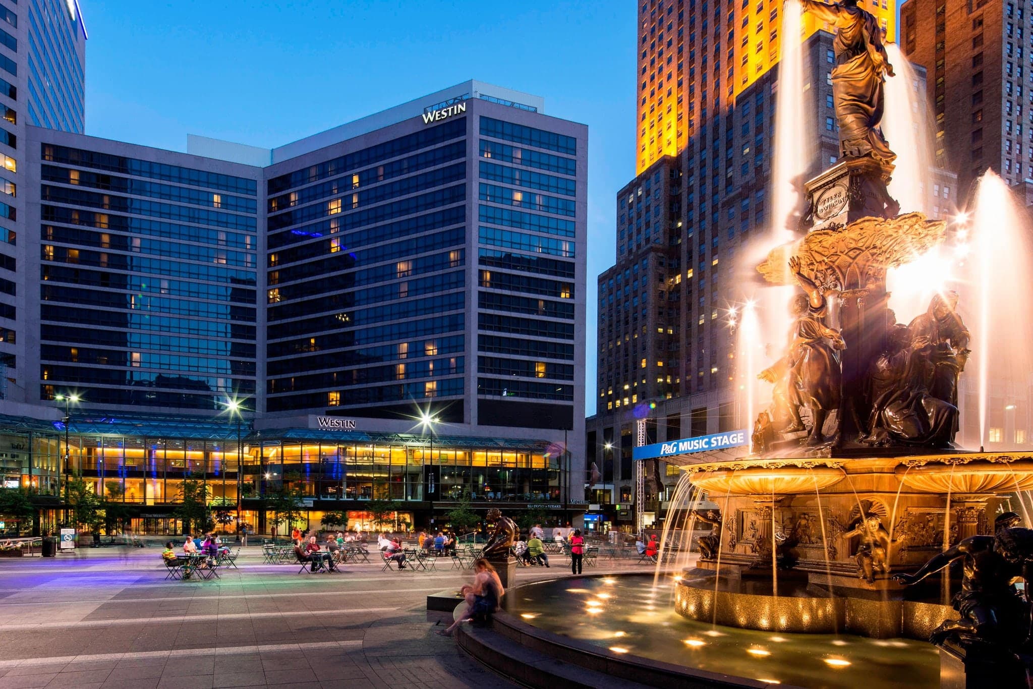 A high-angle view from a hotel window looking down at the illuminated Tyler Davidson Fountain in Cincinnati's Fountain Square at twilight.