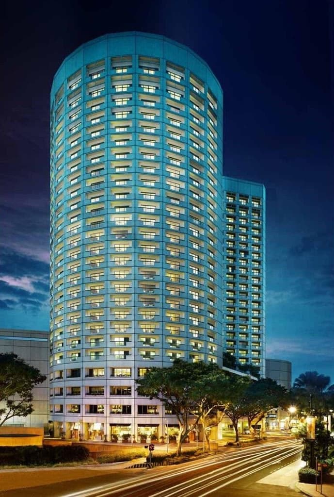 A guest standing on a private balcony at Fairmont Singapore, overlooking the illuminated Marina Bay Sands and ArtScience Museum at night.