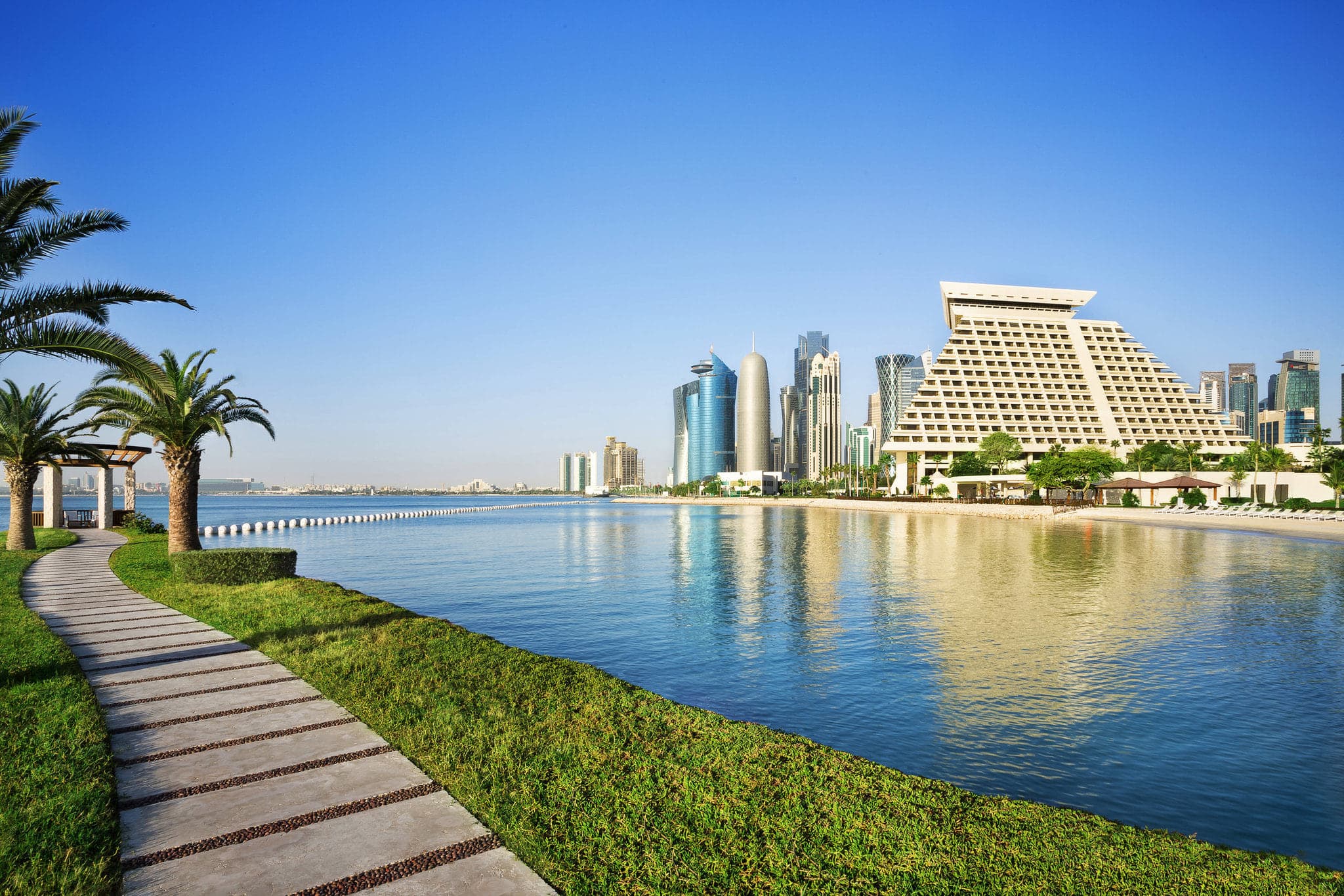 The iconic pyramid shape of the Sheraton Grand Doha reflected in the water at twilight.