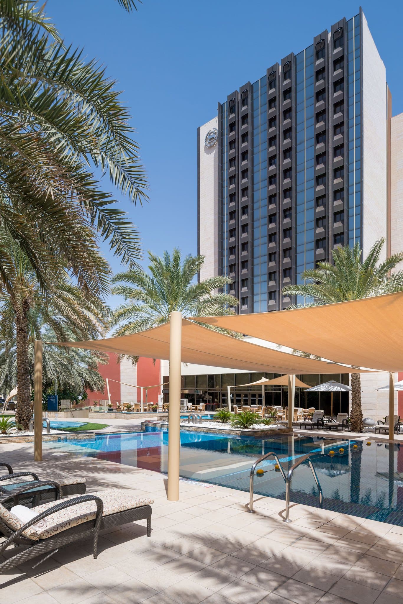 A dramatic low-angle shot of the Sheraton Oman Hotel's tower against the rugged Al Hajar Mountains, highlighting its status as the tallest hotel in Muscat.