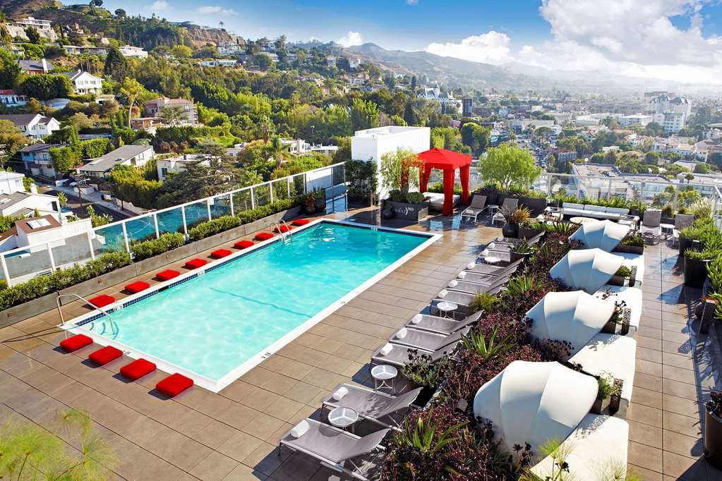 Andaz West Hollywood rooftop pool deck with guests lounging on daybeds, overlooking the Los Angeles skyline at sunset.