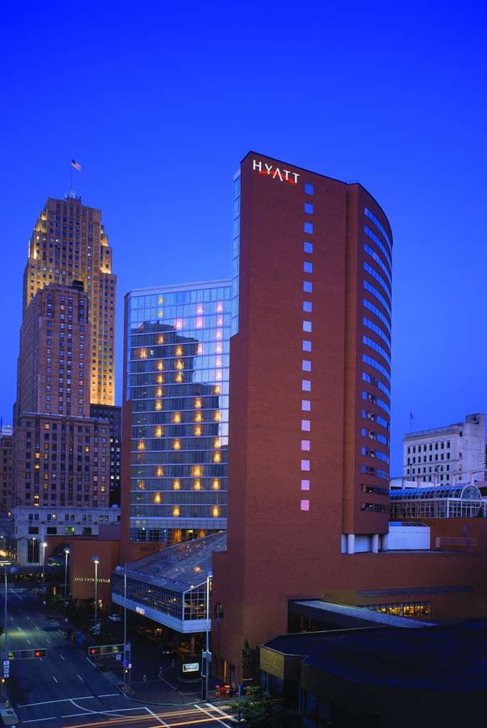 A high-angle shot of the Hyatt Regency Cincinnati indoor saltwater pool enclosed in a glass dome, with downtown skyscrapers visible through the ceiling panels.