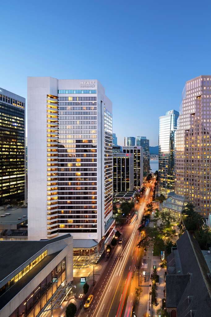 A sleek, modern hotel room balcony at Hyatt Regency Vancouver overlooking the city skyline during golden hour.