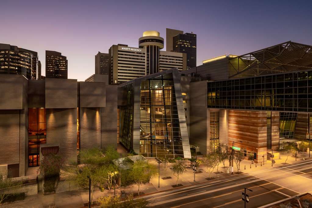 A dramatic low-angle shot of the Hyatt Regency Phoenix's Brutalist concrete exterior at twilight, featuring the illuminated, disc-shaped Compass Arizona Grill revolving restaurant on the rooftop.