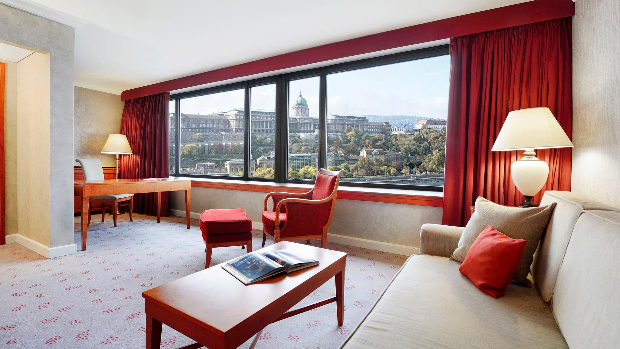 A guest sitting on a window ledge in an InterContinental Budapest suite, gazing out at the illuminated Buda Castle and Chain Bridge at twilight.