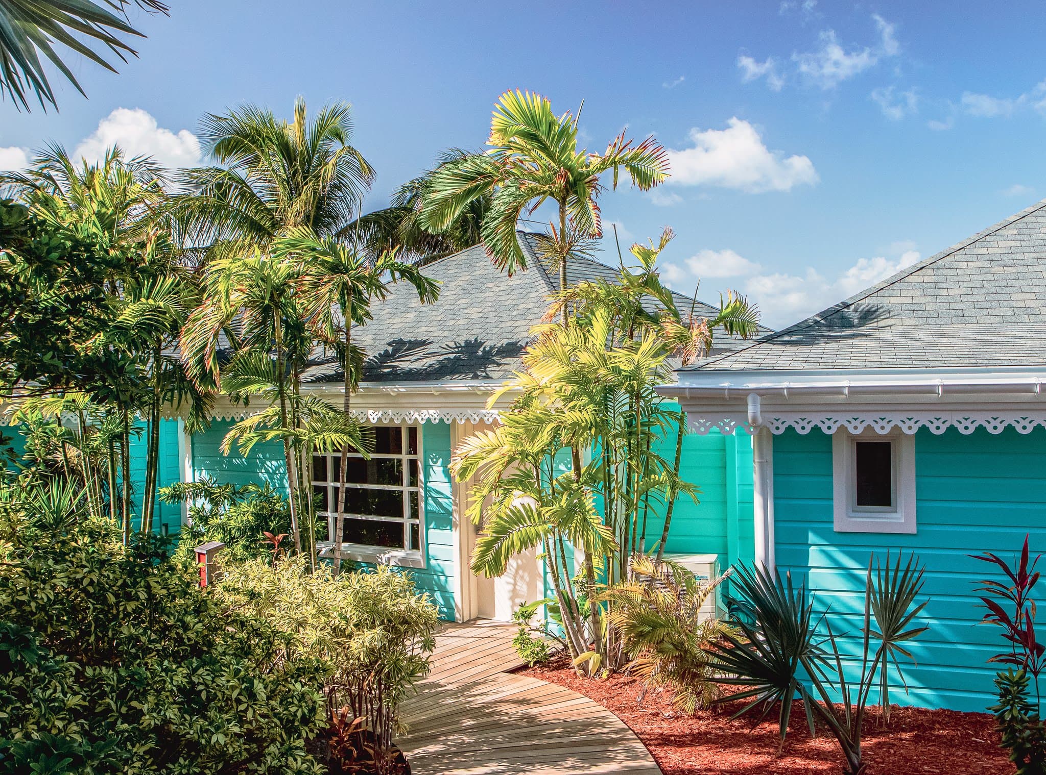 Vibrant turquoise and yellow cottages of Rosewood Le Guanahani St. Barth surrounded by lush bougainvillea and palm trees.