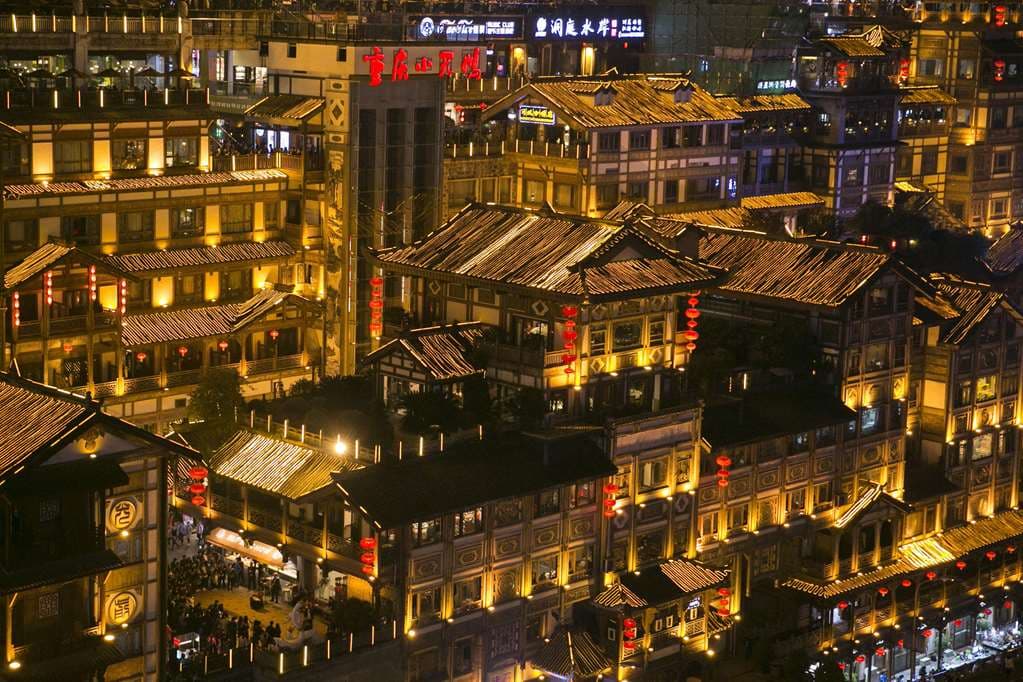 A dramatic view of the Hilton Chongqing's rooftop truss structure illuminated against the night sky, contrasting with the city lights.