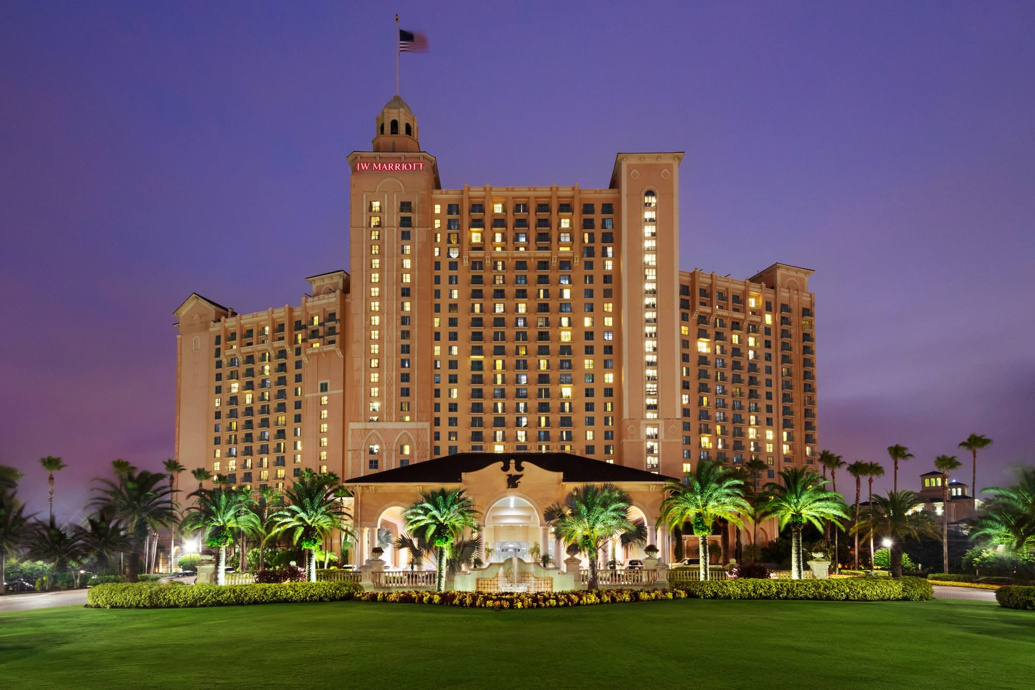 The JW Marriott Orlando Grande Lakes outdoor pool complex at sunset, featuring the lazy river and the Headwaters Slide Tower framed by palm trees.