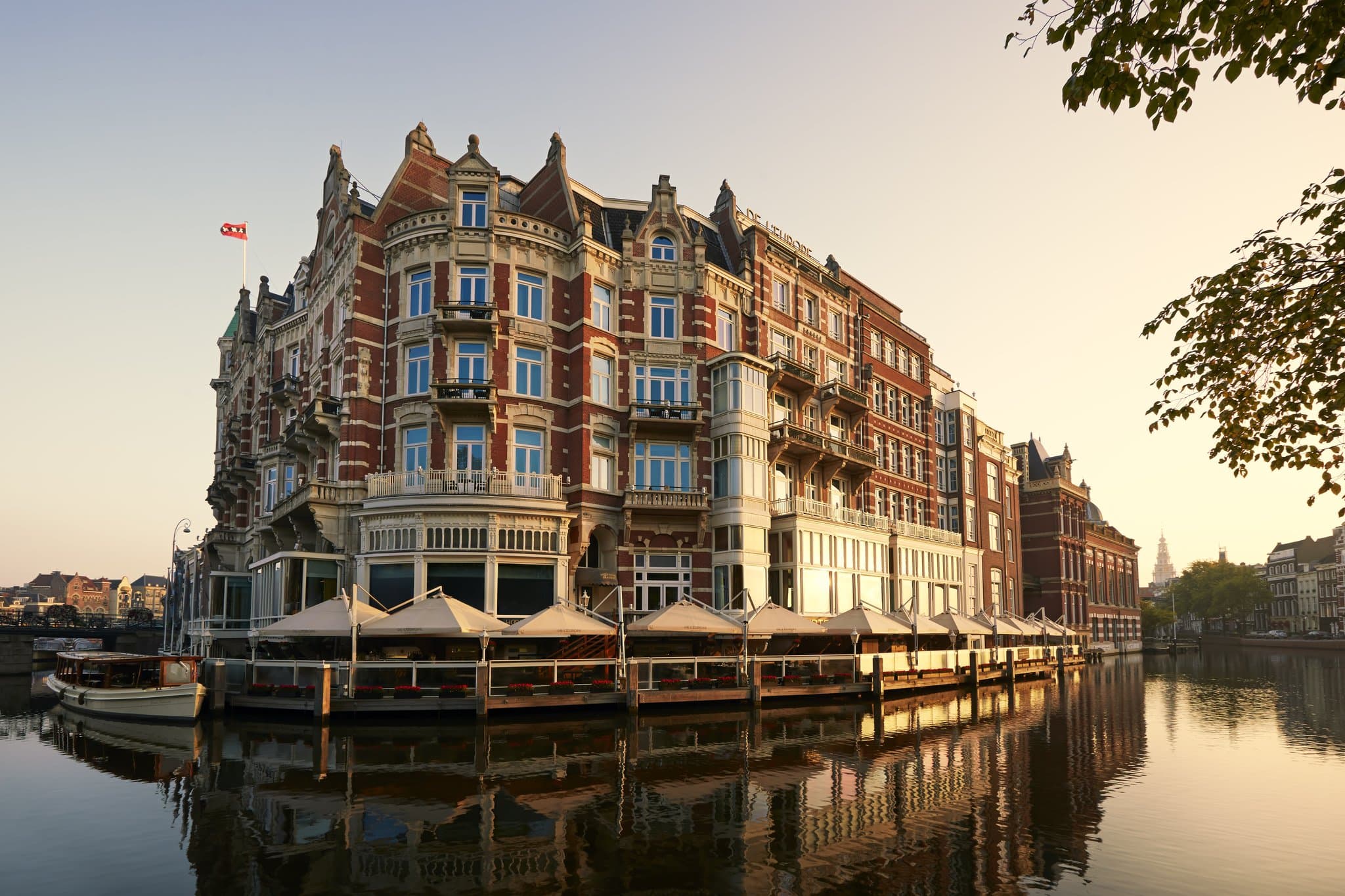 The expansive terrace of Brasserie Marie at De L'Europe Amsterdam, set directly on the Amstel River with boats passing by.