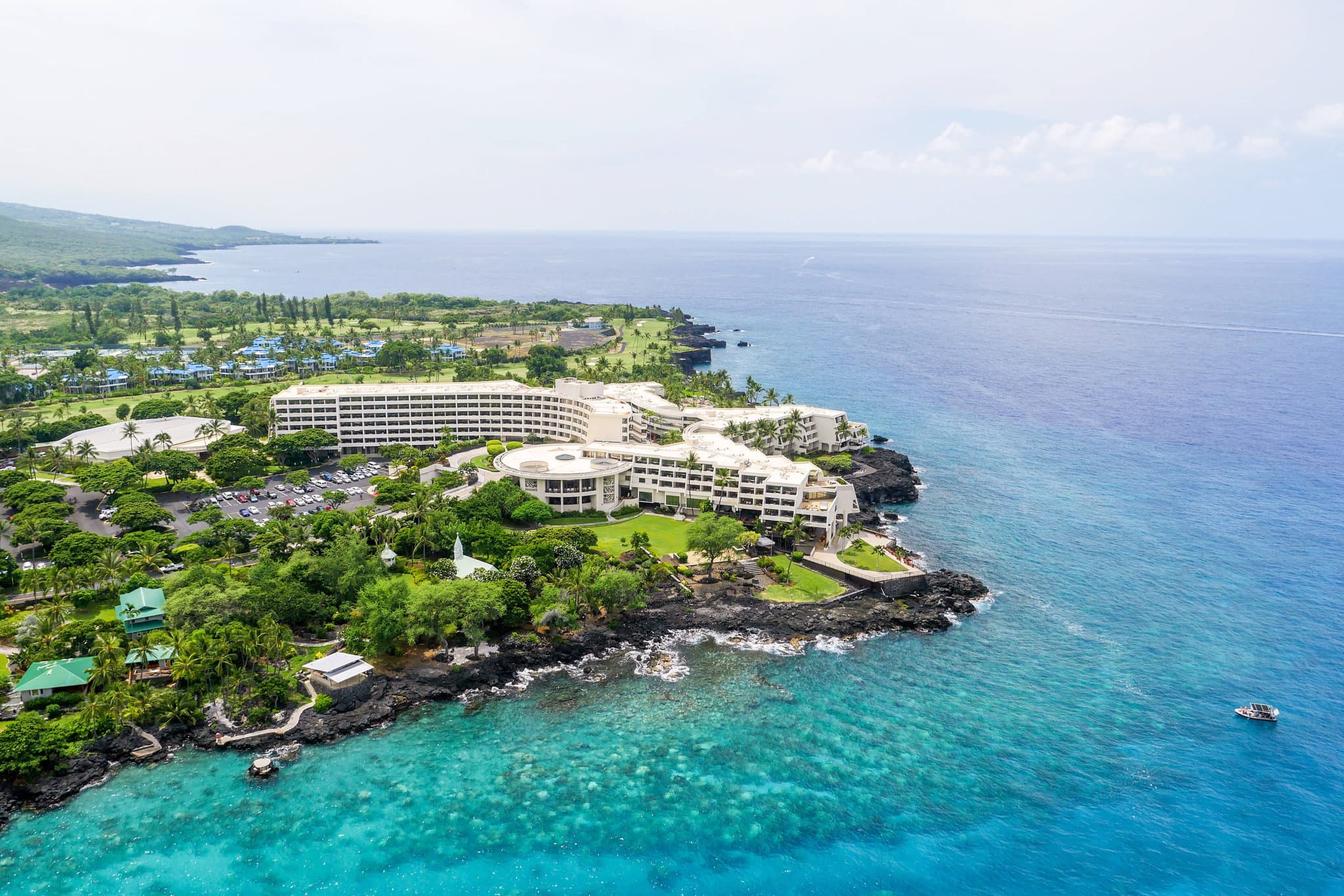 Night view of the Outrigger Kona Resort's illuminated lava cliffs with manta rays visible in the water below.