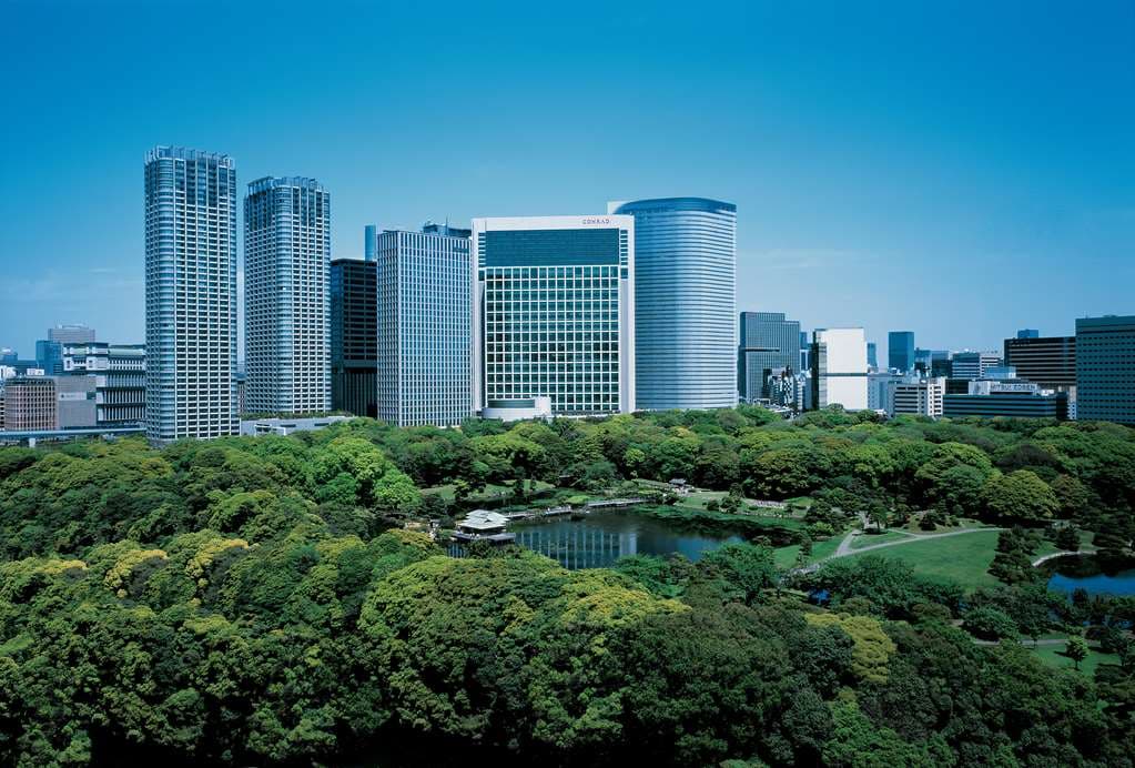 A low-angle shot of the Conrad Tokyo's TwentyEight bar at dusk, featuring floor-to-ceiling windows overlooking a twinkling Tokyo Bay skyline.