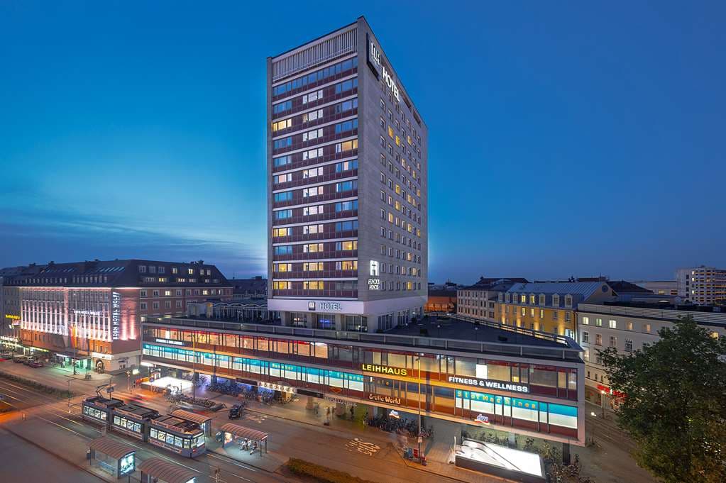 A chic, modern hotel room at NH Collection München Bavaria featuring a large window with a view of the Munich skyline and the Alps in the distance.
