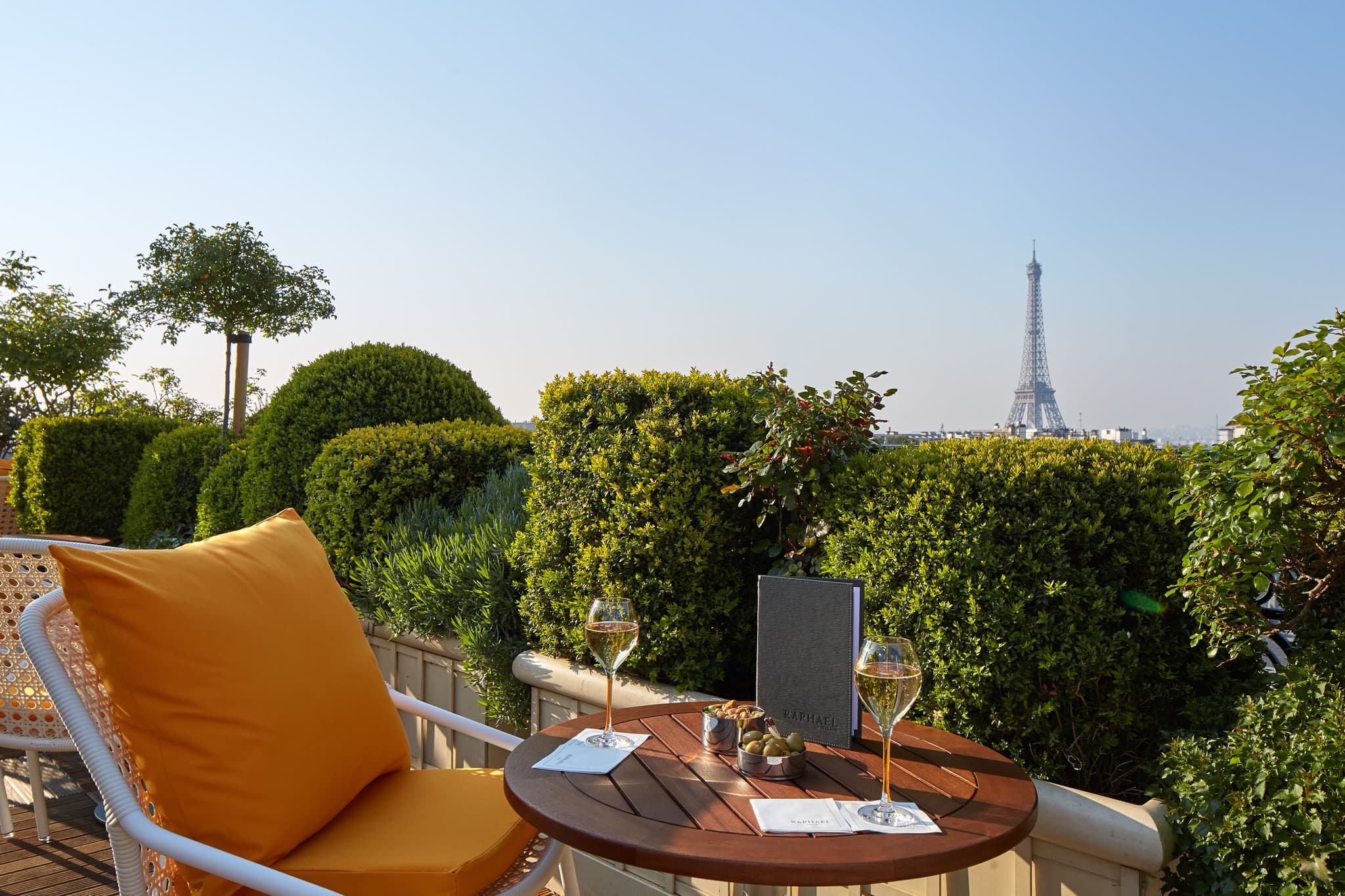 A guest sipping champagne on the Hotel Raphael rooftop terrace with a close-up view of the Eiffel Tower behind them.