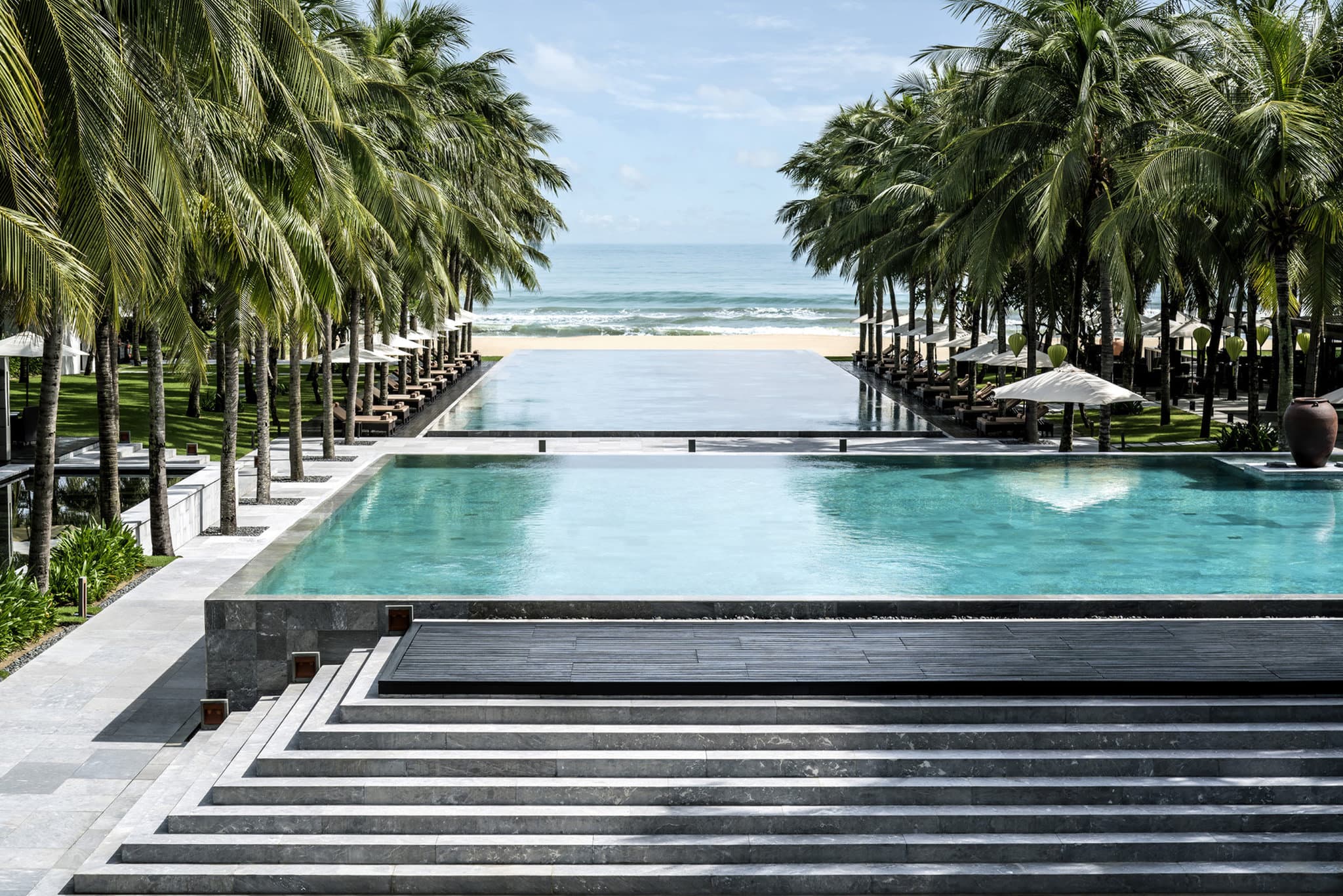 Symmetrical infinity pools at Four Seasons Nam Hai leading the eye toward the palm-fringed Ha My Beach at dusk.