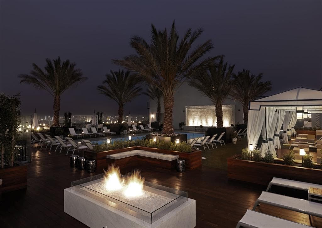 Rooftop pool deck at The London West Hollywood featuring private cabanas, lounge chairs, and a panoramic view of the Los Angeles skyline during the day.