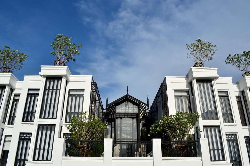 The Siam hotel main atrium featuring a black and white Art Deco design, reflecting pool, and lush tropical greenery under a glass pyramid roof.