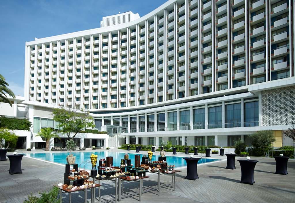 The Ilisian hotel exterior featuring the iconic Yannis Moralis relief facade under distinct Athenian sunlight.