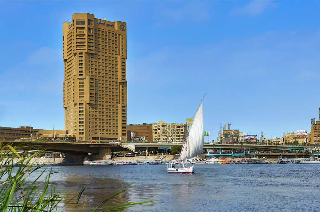 A dramatic dusk view from a high balcony at Ramses Hilton, overlooking the illuminated Nile River with Cairo traffic streaking below.