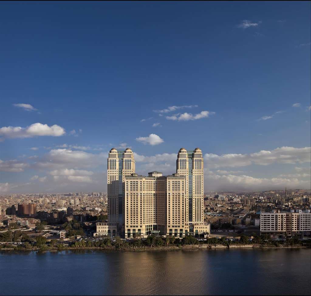 Rooftop Sky Pool at Fairmont Nile City with guests relaxing on loungers, overlooking the River Nile and distant Pyramids at sunset.