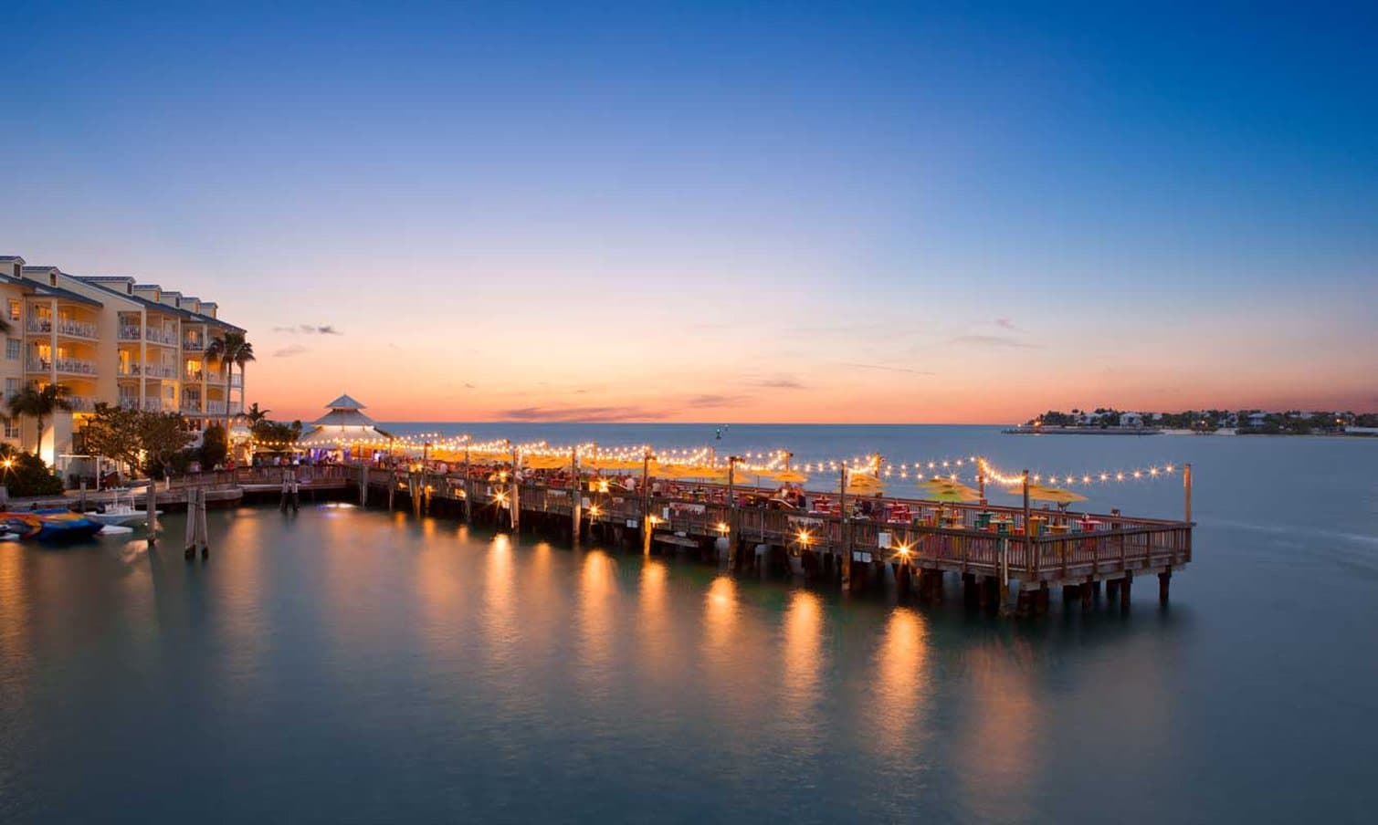 A couple enjoying a private sunset dinner on the balcony of Ocean Key Resort, overlooking the Gulf of Mexico with a vibrant orange sky.