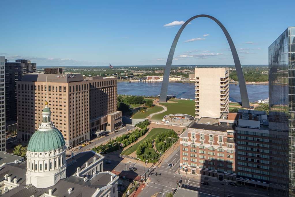 A guest room window framing a close-up, dramatic view of the Gateway Arch against a blue sky.