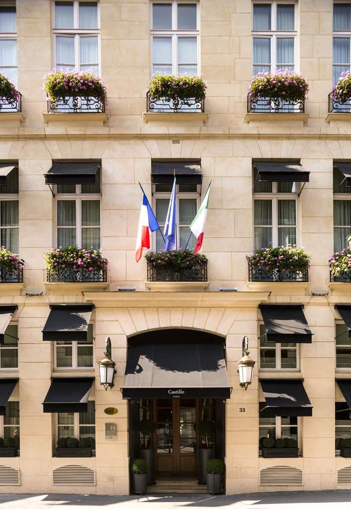 Castille Paris 酒店的罗马式庭院,设有石制喷泉、错视画风格壁画和爬满常春藤的墙壁,摆放着 L'Assaggio 餐厅的餐桌。