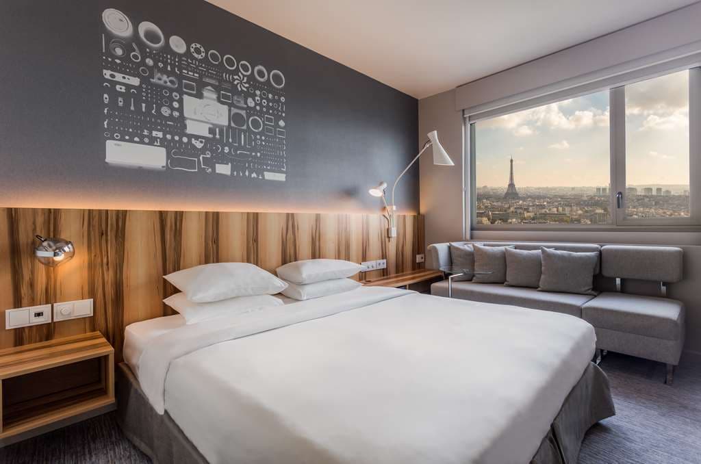 A guest sipping a cocktail at Windo Skybar on the 34th floor, with the illuminated Eiffel Tower dominating the night skyline through floor-to-ceiling windows.